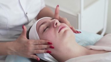 Güzellik uzmanının elleri kanepede gözleri kapalı yatan bir kadının yüzüne krem sürüyor. Güzellik salonu müşterisi profesyonel cilt bakımı alıyor. Refah kavramı