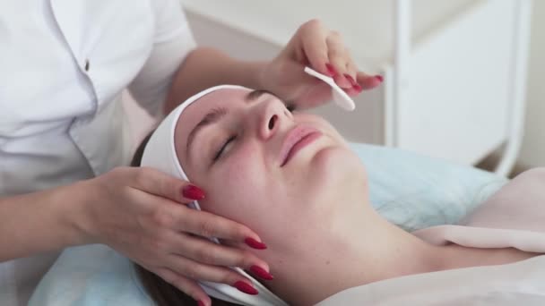 Kozmetológus orvos törölje nő arcát használ pamut párna után hámozási eljárás. Az orvos kozmetikai beavatkozást végez a kozmetikai klinikán.. — Stock videók