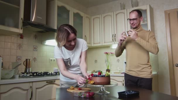 Hausfrau dekoriert Schokoladenkuchen mit Beeren, und ihr Mann macht ein Video davon — Stockvideo