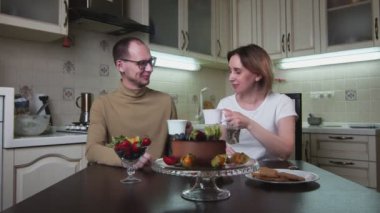 Yetişkin çift mutfakta oturur, konuşur ve çay içer.