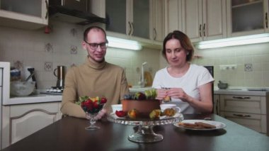 Yetişkin çift mutfakta oturur, konuşur, çay içer ve kurabiye yer.