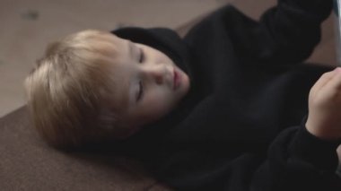 Siyah kapüşonlu şirin çocuğun kanepede yatıp tablet kullandığına yakın çekim. Küçük el kamerası sallaması