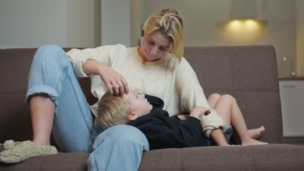 Szczęśliwy mały chłopiec w czarnej bluzie leży na kanapie z matką i rozmawia z nią — Wideo stockowe