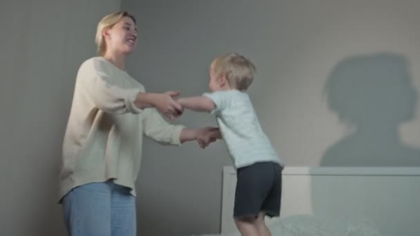 Щасливий хлопчик стрибає в ліжку зі своєю матір'ю вночі вдома — стокове відео