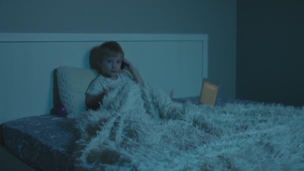 Pequeño hombre de negocios chico utiliza el ordenador portátil y habla por teléfono en la cama por la noche — Vídeo de stock