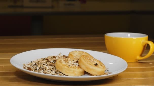 Sýrové křupky Syrniki na talíři s granolou a žlutým šálkem čaje — Stock video
