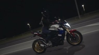 Kameraya bakan ve geceleri otoyolda motosiklet süren bir kadının yan görüntüsü.