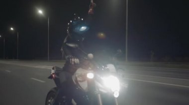 Siyah kasklı genç bir kadın motosiklete biniyor ve elinde asansörle yukarı çıkıyor.