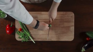 Erkekler, tahta bir tahtanın üzerinde bir salatalığı bıçakla keserler.