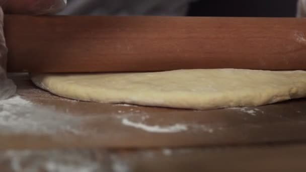 Руки профессионального пекаря выкатывают тесто со скалкой на столе с мукой. — стоковое видео