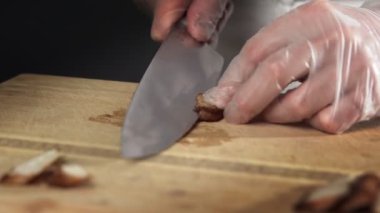 Şef bıçak tutuyor, hazırlanmış sulu biftekleri kesiyor.