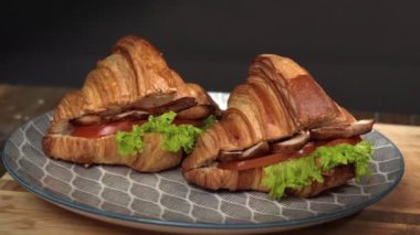 İki tane etli ve sebzeli kruvasan sandviçi. Kahvaltı konsepti. Tabağında et ve sebze olan sandviçler. Kahvaltı konsepti..