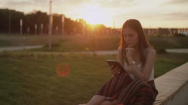 Gün batımında parkta bir kız e-kitap okuyor.