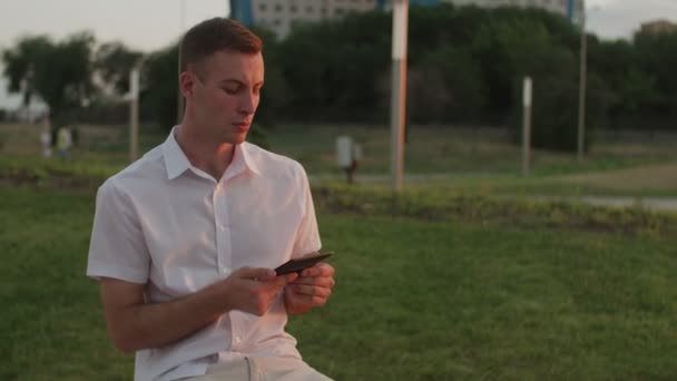 Вечером парень на улице читает электронную книгу — стоковое видео