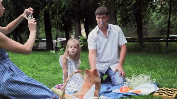 Padre e hija juegan con el perro en un picnic en el parque, y sus fotos madre en el teléfono — Vídeos de Stock