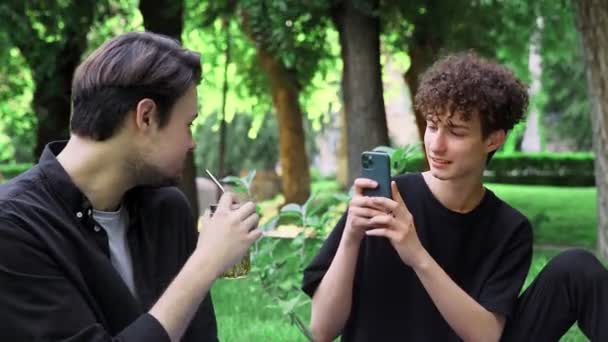 한 남자가 여름에 자연에 있는 다른 남자의 전화로 사진을 찍습니다. — 비디오
