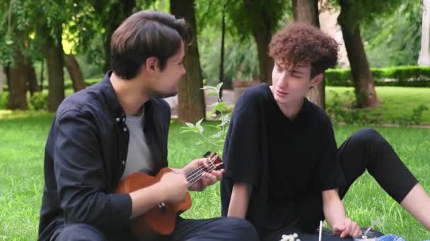 Um cara toca ukulele para outro cara na natureza no verão — Vídeo de Stock