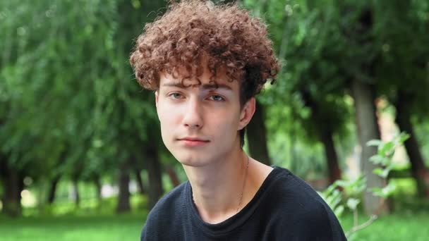 Młody kręcone włosy facet patrzy smutno w obiektyw w przyrodzie w lecie — Wideo stockowe