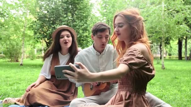 Dziewczyna nagrywa filmik przez telefon, kiedy ona i jej przyjaciele śpiewają piosenki w naturze latem. — Wideo stockowe
