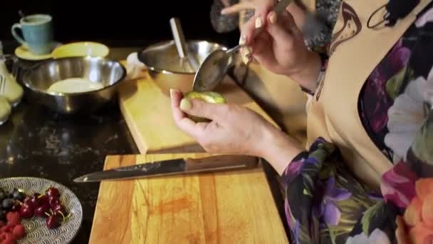 Uma mulher limpa um abacate com uma colher na cozinha — Vídeo de Stock
