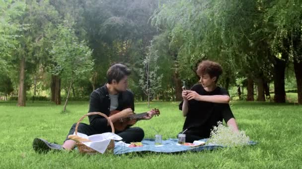 A guy plays the ukulele to another guy in nature in the summer — Stock Video