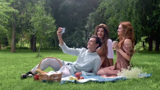 Un chico y dos chicas son fotografiados por teléfono en un picnic en verano en la naturaleza — Vídeos de Stock