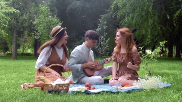 Un chico toca un ukelele, y las chicas cantan una canción en la naturaleza en el verano — Vídeos de Stock