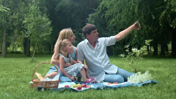 Un hombre toma fotos de sí mismo, un niño y una mujer en un picnic de verano en la naturaleza — Vídeos de Stock