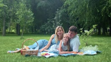 Aile yazın doğada bir battaniyeye uzanır ve fotoğraf için poz verir.