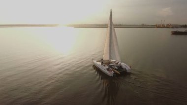 Küçük bir yelkenli yat gün batımında nehirde yelken açar.