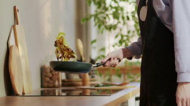 Şef, elleri tavada, elektrikli sobada yağlı bir tabak hazırlar.