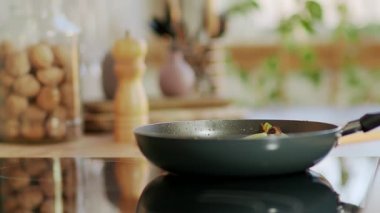 Şef elektrikli ocakta tavaya otlar serpiyor.