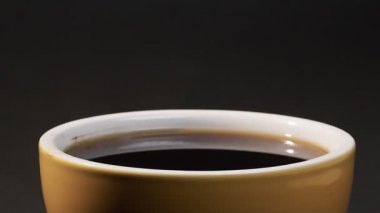 Bir damla çay, siyah arka planda dolu bir bardak çaya damlıyor.