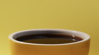 Sarı arka planda bir bardak çay bardağına damlayan bir damla çay.