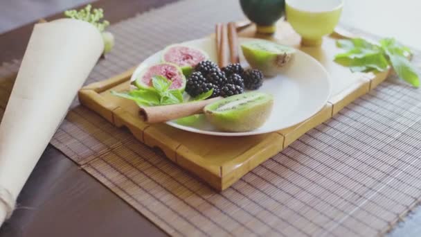 Délicieux plat de fruits sur une assiette avec thé vert parfumé sur un plateau en bois — Video