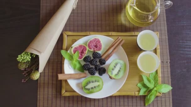 Pyszne danie owocowe na talerzu z pachnącą zieloną herbatą na drewnianej tacy — Wideo stockowe