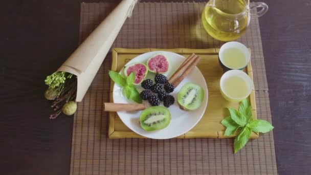 Delicioso plato de frutas en un plato con té verde fragante en una bandeja de madera — Vídeos de Stock