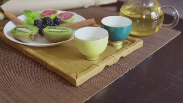 Mâncare delicioasă de fructe pe o farfurie cu ceai verde parfumat pe o tavă de lemn — Videoclip de stoc