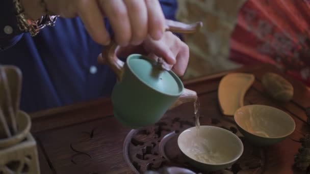 Een man giet thee in theekopjes op een houten dienblad in een theekamer — Stockvideo