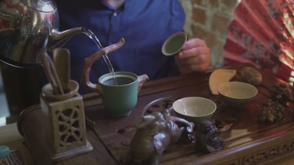 Een man giet kokend water uit een theepot in een theepot voor thee brouwen in een theekamer — Stockvideo