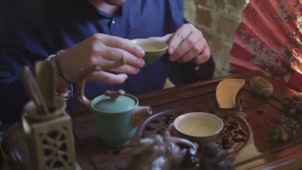 Een man drinkt groene thee uit een theeservies in een theekamer — Stockvideo