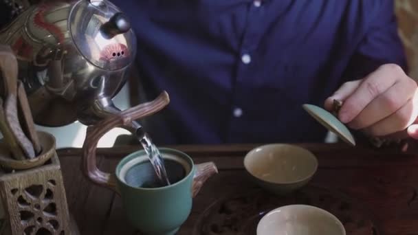 Egy férfi forró vizet önt a teáskannából egy teáskannába, hogy teát főzzön a teázóban. — Stock videók