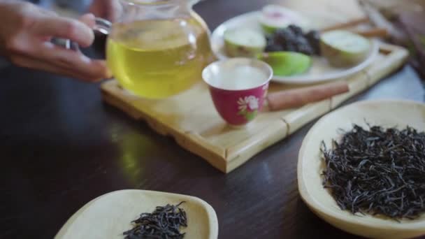 Una mano de mujer vierte té verde en una taza de té sobre la mesa — Vídeos de Stock