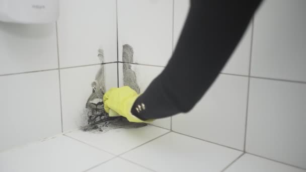 Een vrouwenhand in een gele rubberen handschoen reinigt vuil met een spons op een witte tegel — Stockvideo