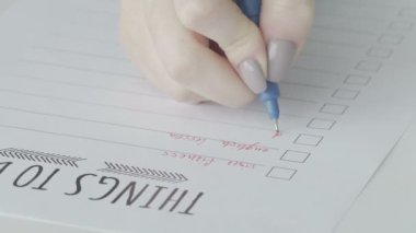 Bir kadının eli yapılacaklar listesine ne yapılması gerektiğini yazar, yakın plan.