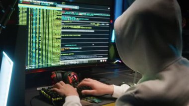 Maskeli bir hacker bilgisayardaki bir veritabanına girip karanlık bir odayı hackliyor.