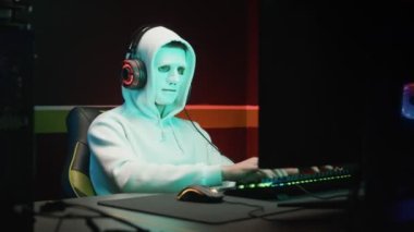 Maskeli bir hacker bilgisayardaki bir veritabanına girip karanlık bir odayı hackliyor.