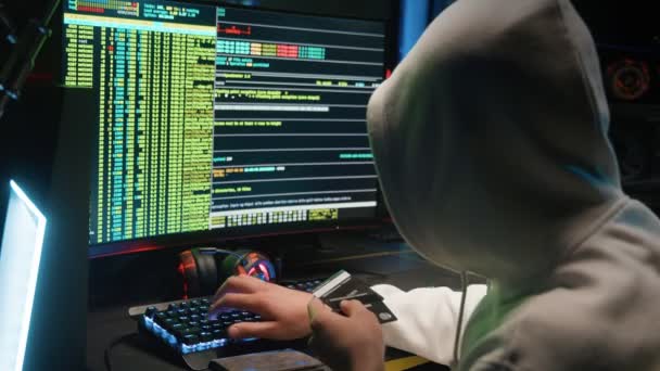 Een gemaskerde hacker breekt in in een database op een computer, hackt in een donkere kamer — Stockvideo