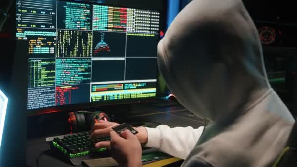 Хакер в маске взламывает базу данных на компьютере, взламывает ее в темной комнате — стоковое видео