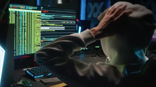 Un hacker mascherato irrompe in un database su un computer, hackerando in una stanza buia — Video Stock